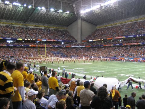 1986 Ford Bronco - A packed football stadium with spectators and a marching band on the field during an event.