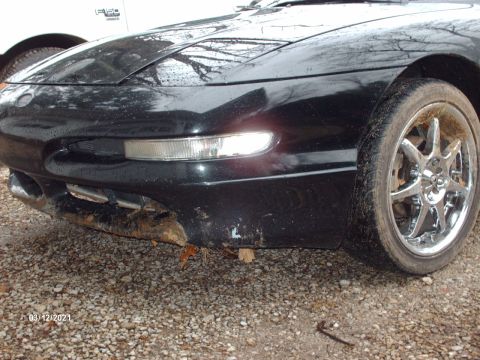 1995 Ford Probe - Front view of a black 1995 Ford Probe showing damage to the bumper and a chrome wheel. Another vehicle is partially visible.