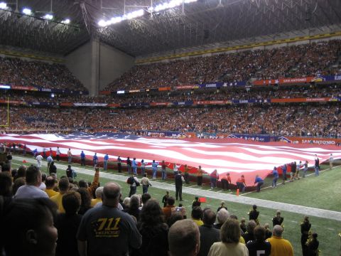 1986 Ford Bronco - Spectators hold a giant American flag on the field during a football game in a stadium.