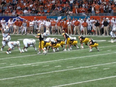 1986 Ford Bronco - Two teams face off on a football field during a game, with spectators in the stands.