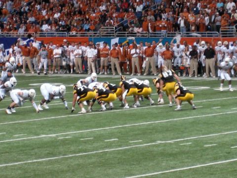 1986 Ford Bronco - A football game is underway with players from two teams lined up on the field, watched by a large crowd in the stands.
