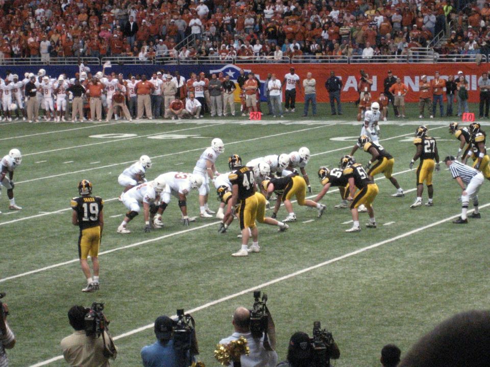 Football players in uniform on a field during a game, with spectators in the background