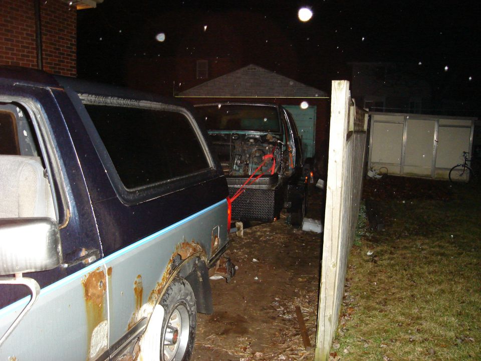 Two SUVs in a yard at night, one with its engine compartment open