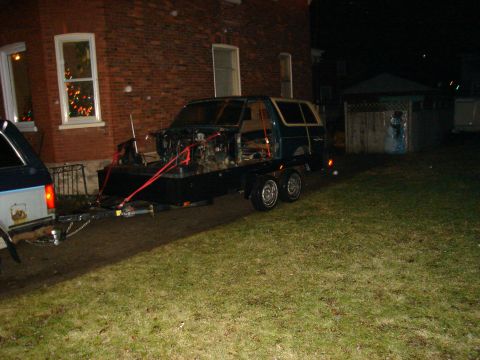 1990 Ford Bronco - A dark green Ford Bronco body is transported on a trailer, its front end disassembled.