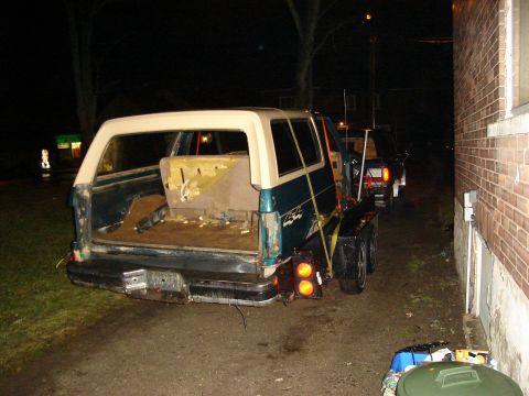 1990 Ford Bronco - A teal and cream SUV, possibly a 1990 Ford Bronco, is seen being towed on a trailer at night.