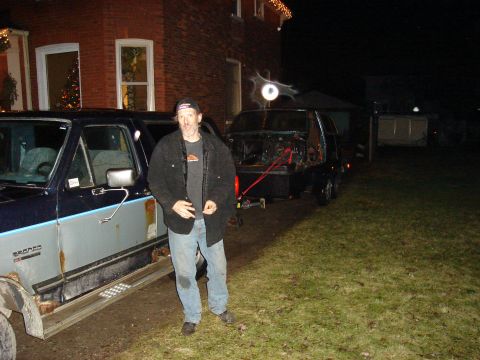 1990 Ford Bronco - Man stands by a rusty 1990 Ford Bronco; another vehicle is visible on a trailer behind.
