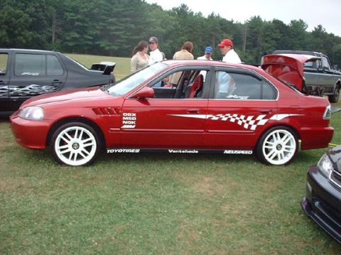 1997 Ford Crown Victoria - A red sedan is parked on grass with other vehicles and people in the background.