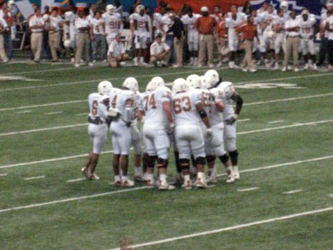 1986 Ford Bronco - Players gather for a huddle on the field during a football game.