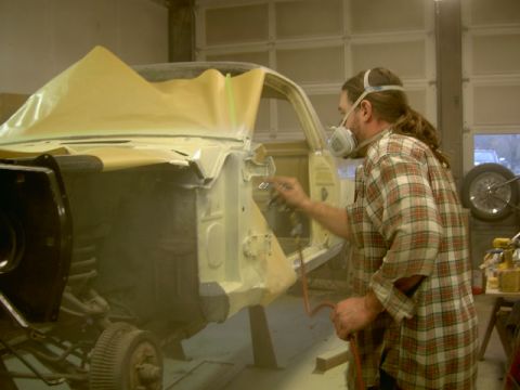 1967 Ford Ranchero - A man in a respirator sprays primer on the body of a 1967 Ford Ranchero in a workshop.