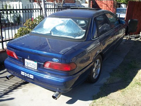 1992 Ford Taurus - Rear view of a blue 1992 Ford Taurus sedan parked in a driveway with dual exhaust pipes visible.