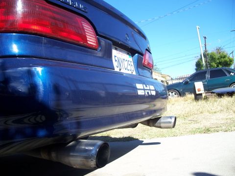 1992 Ford Taurus - Rear view of a blue sedan dual exhaust pipes and a white decal on the bumper, with another vehicle visible in the background.