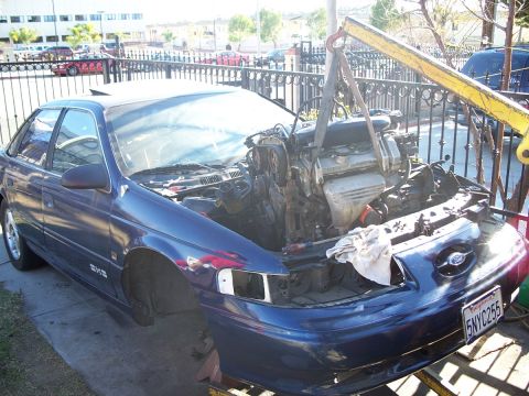 1992 Ford Taurus - A blue Ford Taurus is shown with its engine being removed by a yellow engine hoist.