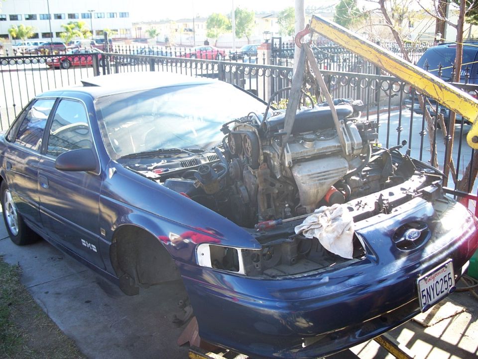 Blue Ford Taurus, engine out and being lifted by a crane. License plate 5NYC255