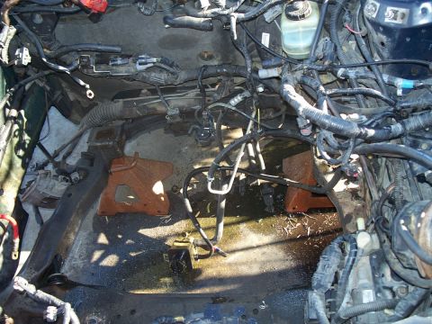1992 Ford Taurus - Disassembled engine bay with exposed wiring and fluid leaks on the floor.