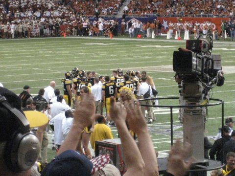 1986 Ford Bronco - A football team huddles on the field during a game, with a large broadcast camera rig in the foreground.