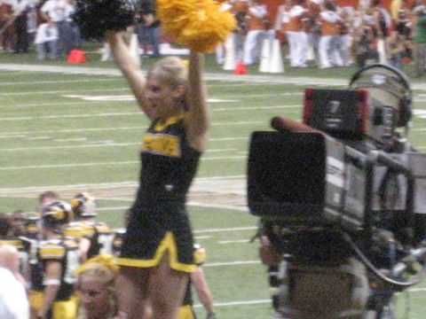 1986 Ford Bronco - A cheerleader performs on the field during a football game, with a camera operator nearby.