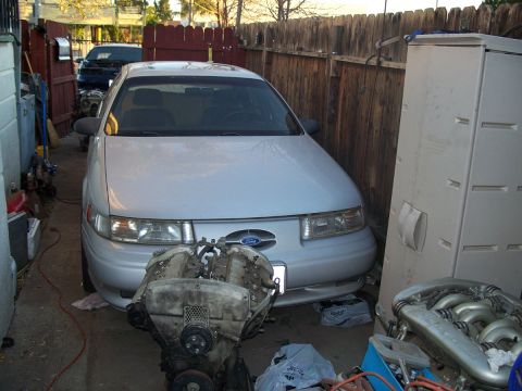 1992 Ford Taurus - A silver 1992 Ford Taurus is parked in a driveway with a disassembled engine in front of it.