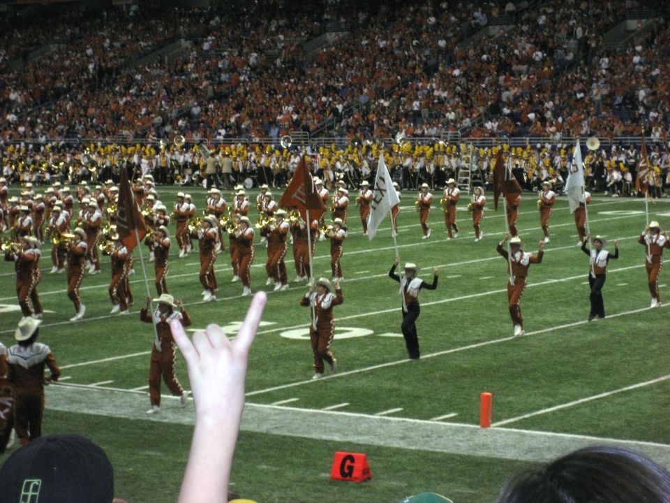 football field with marching band performing, crowd in stands
