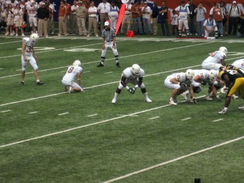 1986 Ford Bronco - Players from two teams prepare for a play on a football field with spectators in the background.