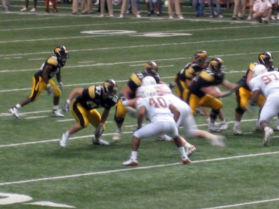 Football players in black and yellow uniforms face off against players in white uniforms on a green field