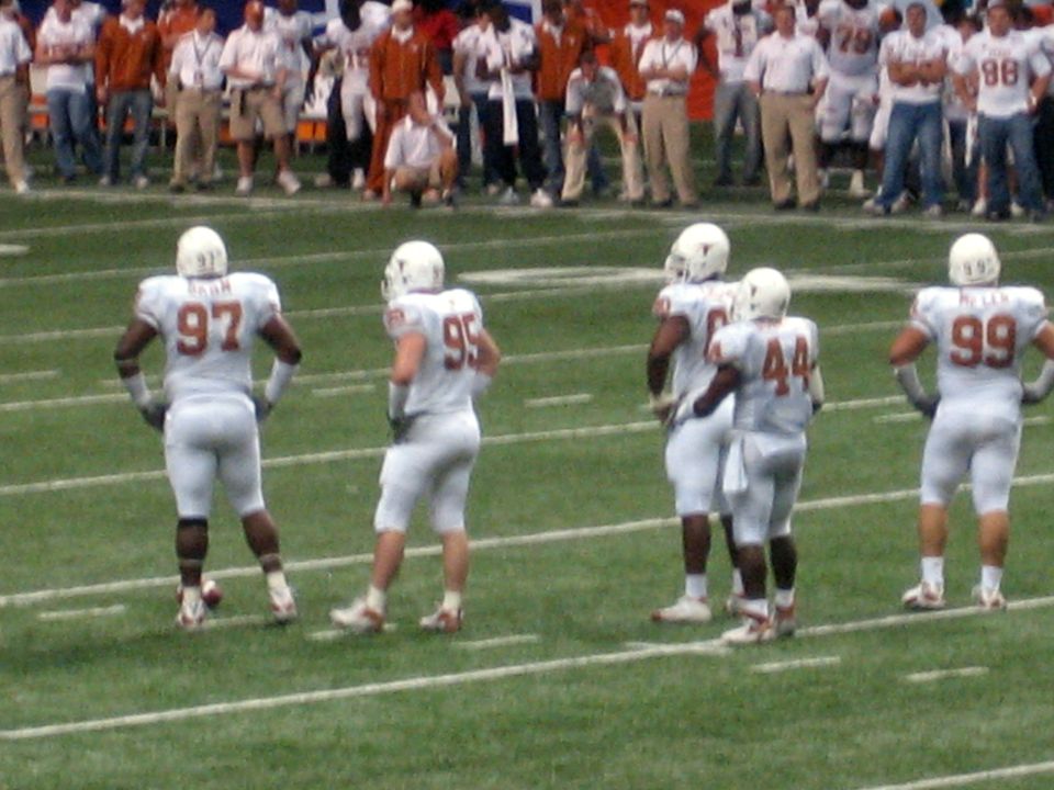 Football players in white uniforms with numbers 97, 95, 44, and 99 on a green field