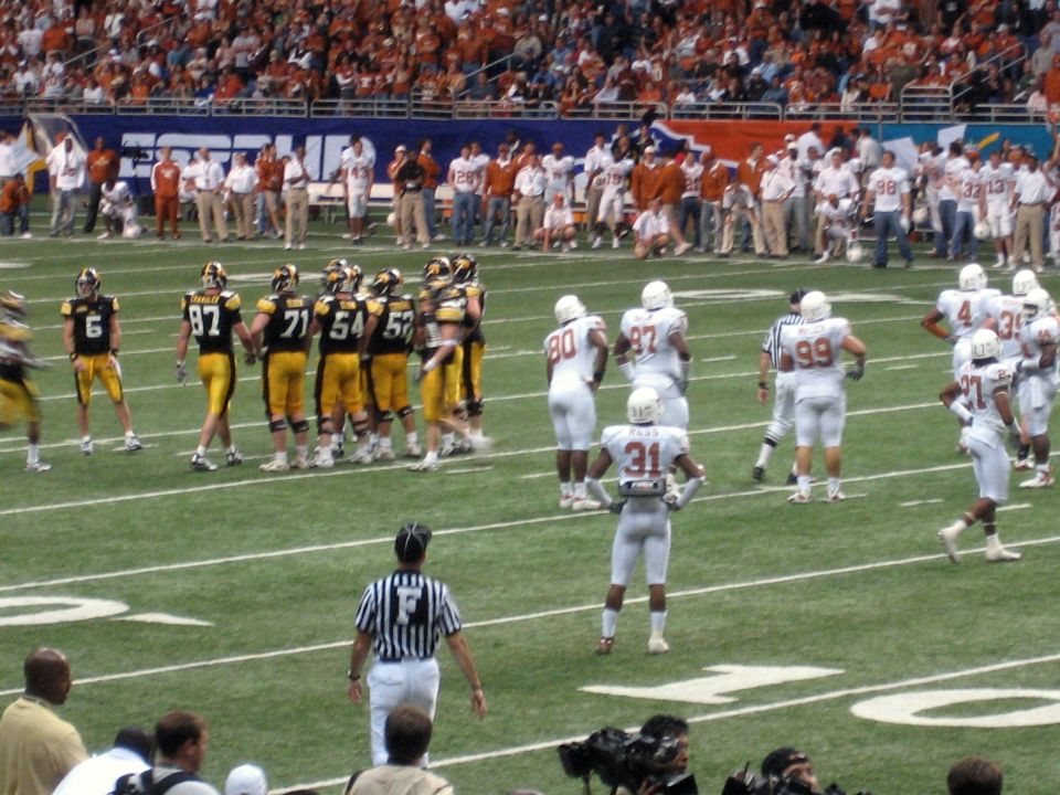 American football game with players in white and black uniforms on the field, spectators in the stands