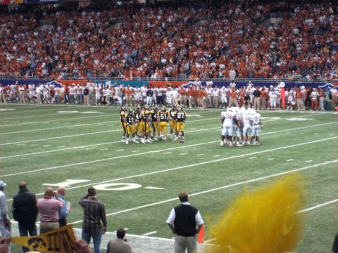 1986 Ford Bronco - Two football teams huddle on the field during a game, with a large crowd in the stands.