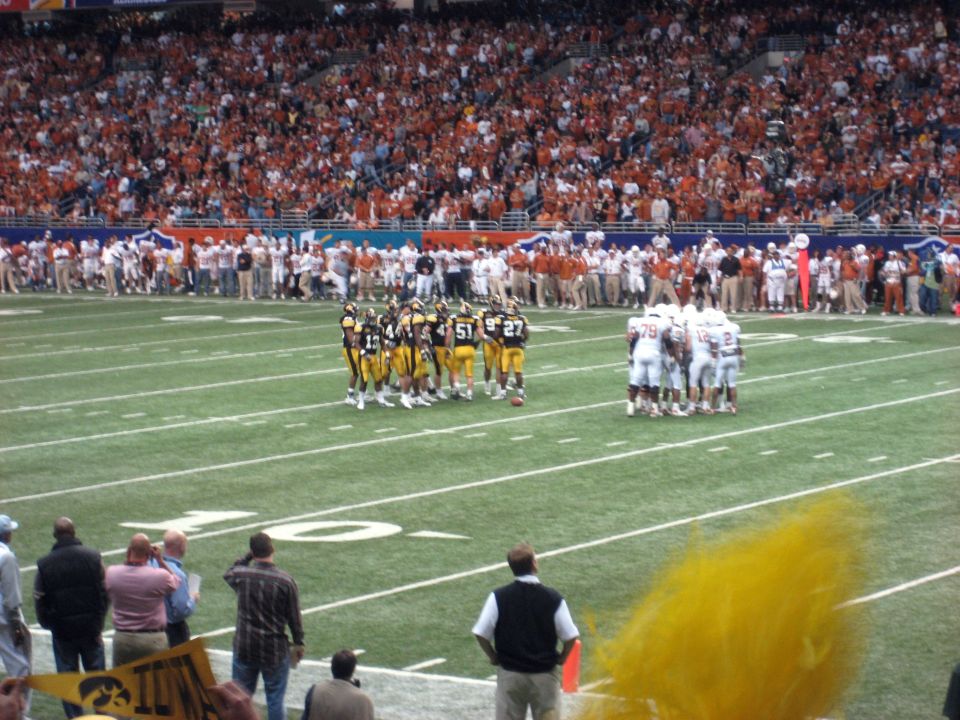 football teams huddle on field during game with packed stands in background
