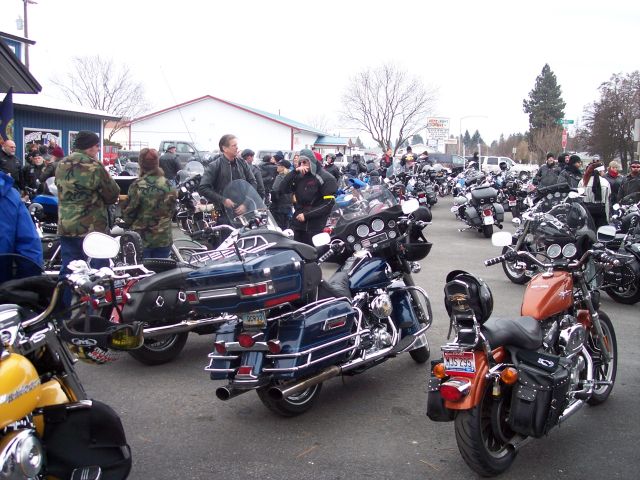 Many motorcycles parked in an outdoor lot with people milling around