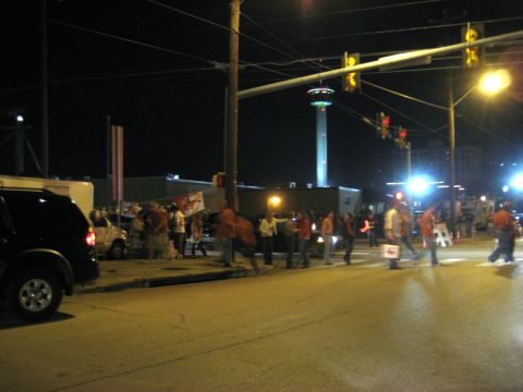 1986 Ford Bronco - A black SUV is parked on the side of a street at night, with a crowd of people and a tower in the background.