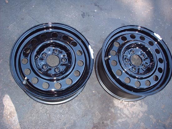 Two black steel wheels with circular cutouts, resting on a textured surface