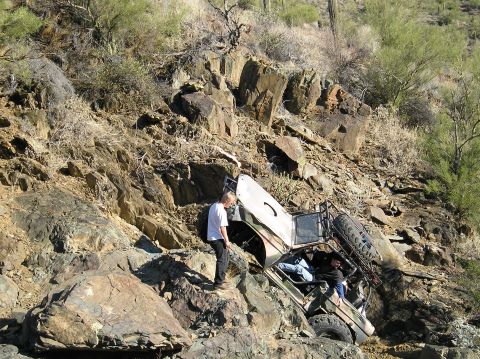 1993 Ford Bronco - An off-road vehicle is precariously positioned on a steep, rocky incline, with two individuals visible inside.