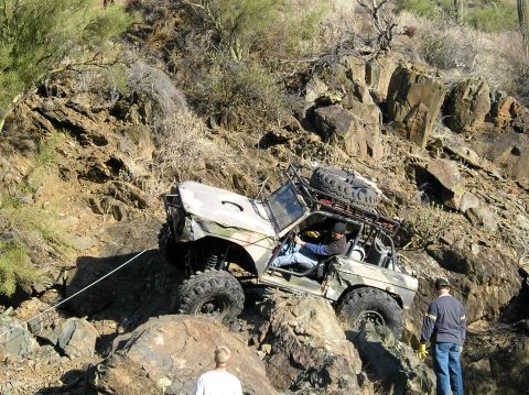 1993 Ford Bronco - An off-road vehicle navigates a steep, rocky incline in a desert environment, with two people observing.