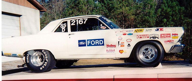 White drag coupe in side view with sponsor decals and rear slicks on a ramp