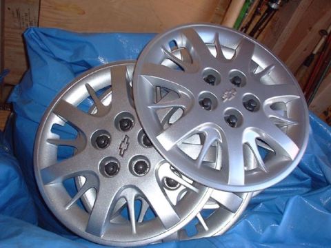 1997 Ford Crown Victoria - Two silver hubcaps, each a Chevrolet bowtie emblem, are shown resting on a blue tarp.