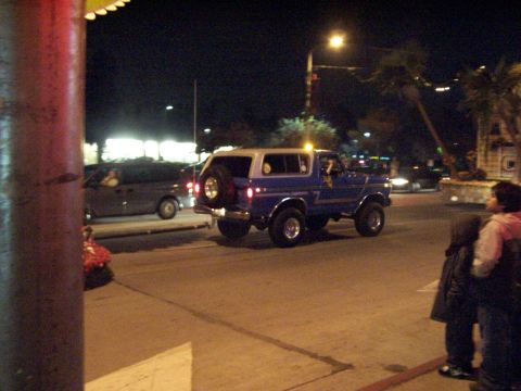 1990 Ford Bronco - A blue Ford Bronco is seen driving at night with a spare tire mounted on its rear.