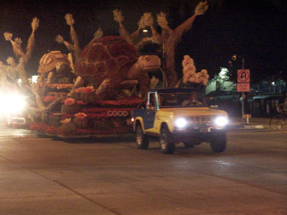 Yellow and blue Ford Bronco driving at night with a float in the background