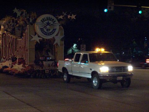 1990 Ford Bronco - A white Ford F-Series pickup truck with amber lights on the roof drives at night.