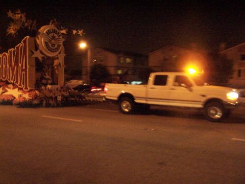 1990 Ford Bronco - A pickup truck tows a float during a nighttime parade event.