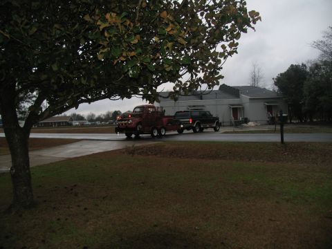 1952 Ford Pickup - A vintage red tow truck, likely from the 1950s, is seen towing a black SUV on a cloudy day.