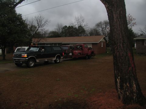 1952 Ford Pickup - A red pickup truck from the early 1950s is being towed by a dark SUV on a cloudy day.