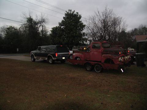 1952 Ford Pickup - A red tow truck transports a black SUV on a trailer under an overcast sky.