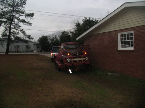 1952 Ford Pickup - A red 1952 Ford Pickup truck is parked on a trailer next to a brick building.