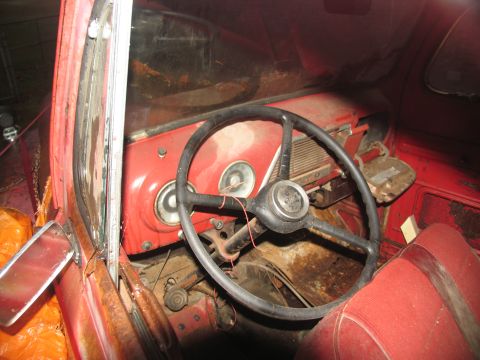 1952 Ford Pickup - The interior of a red pickup truck is visible, a black steering wheel and a red dashboard with gauges.