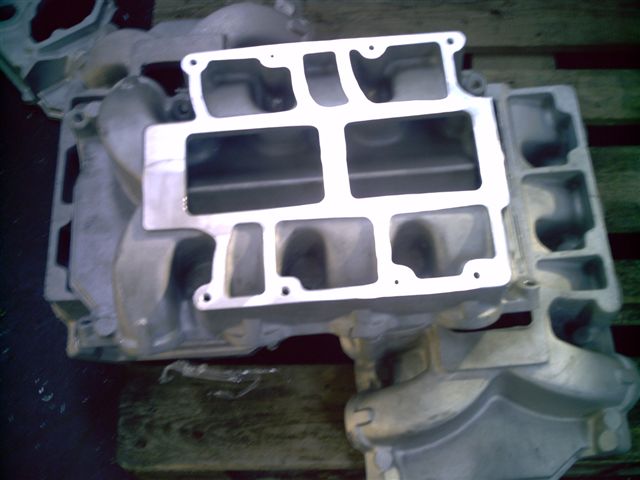 Top view of an aluminum dual-quad intake manifold with machined carb flanges on a pallet
