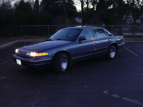 1996 Ford Crown Victoria - This 1996 Ford Crown Victoria sedan is parked in an asphalt lot with trees and a fence in the background.