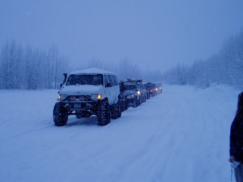 2000 Ford E350 - A convoy of modified off-road vehicles, including a white van, navigates a snow-covered road.