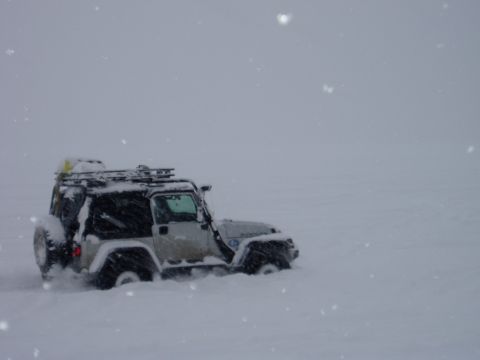 2000 Ford E350 - A Jeep Wrangler is partially buried in snow, with a roof rack carrying gear.