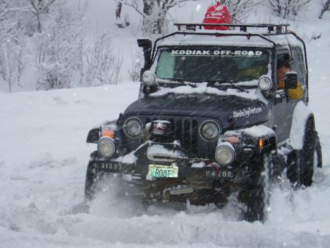 2000 Ford E350 - A Jeep Wrangler navigates a snowy terrain, displaying an "Alaska Jeep Parts.com" decal and "KODIAK OFF-ROAD" banner.