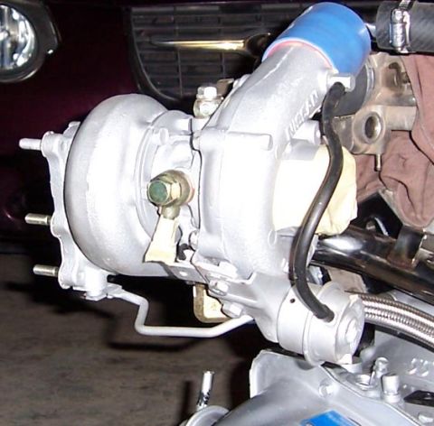 1988 Pontiac Fiero - Close-up of a silver turbocharger with blue intake hose and 'NISSAN' branding, part of an engine assembly.